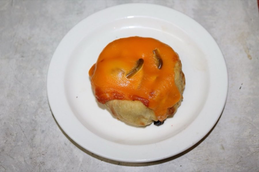 A round knish topped with cheddar cheese, on a white plate