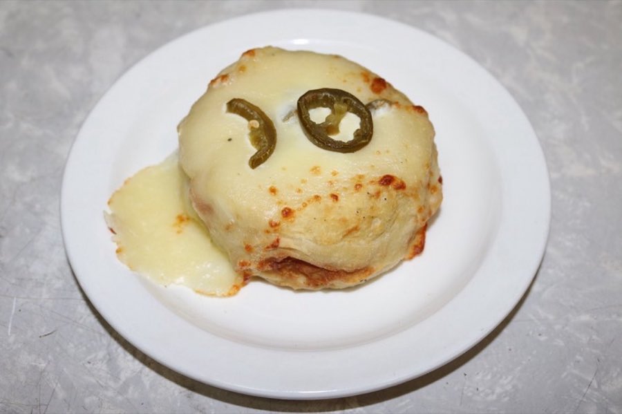 A round knish topped with melted mozzarella cheese, on a white plate