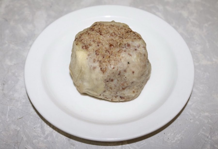 A round baked kasha knish with a browned, speckled buckwheat top, on a white plate