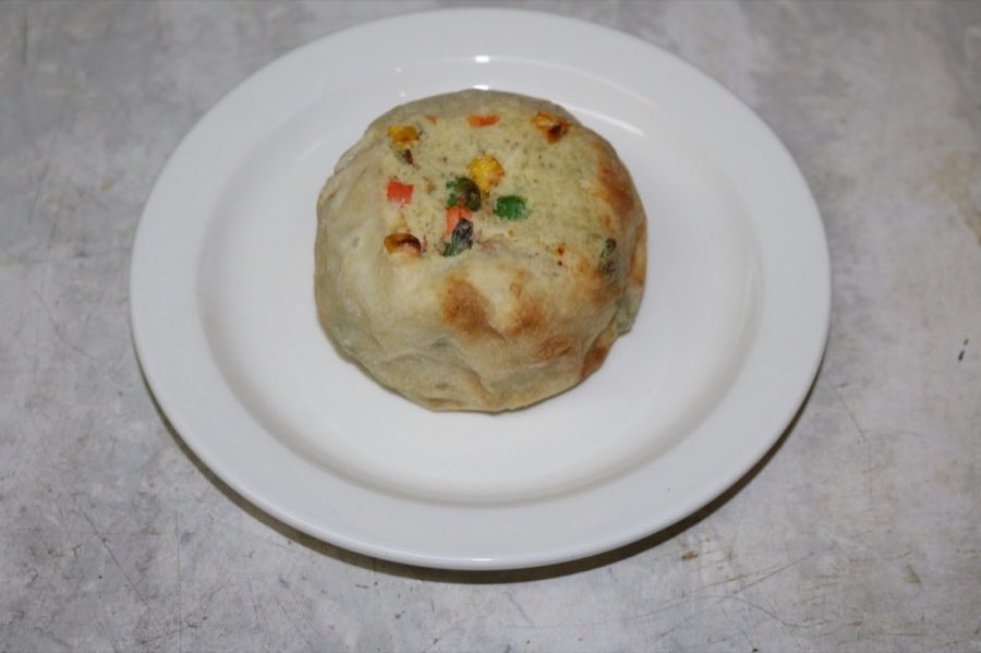 A round baked knish with mixed vegetables visible, on a white plate