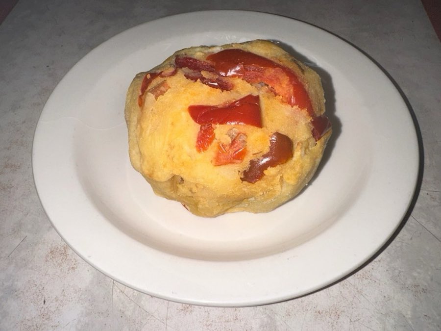 A round knish with peppers and onion topping visible, on a white plate