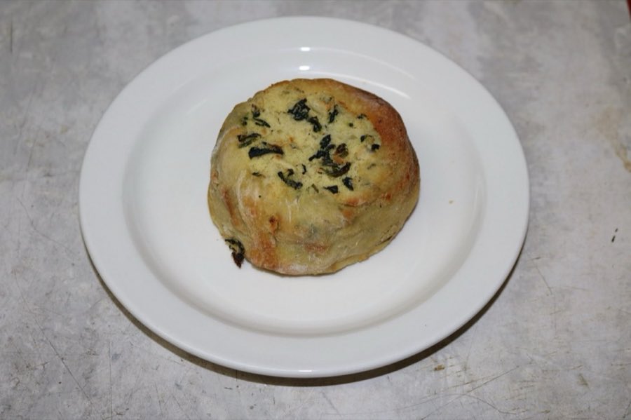 A round baked spinach and potato knish, on a white plate