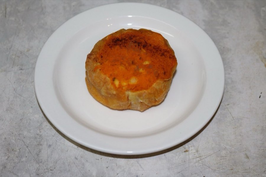 A round baked sweet potato knish with orange filling visible, on a white plate