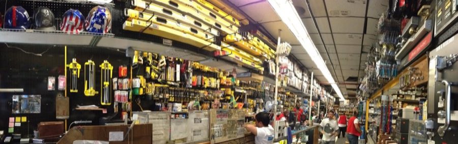 Inside Metropolitan Lumber's crowded store aisle: pegboard walls packed with hand tools, yellow levels racked overhead, and staff in red aprons working the counter