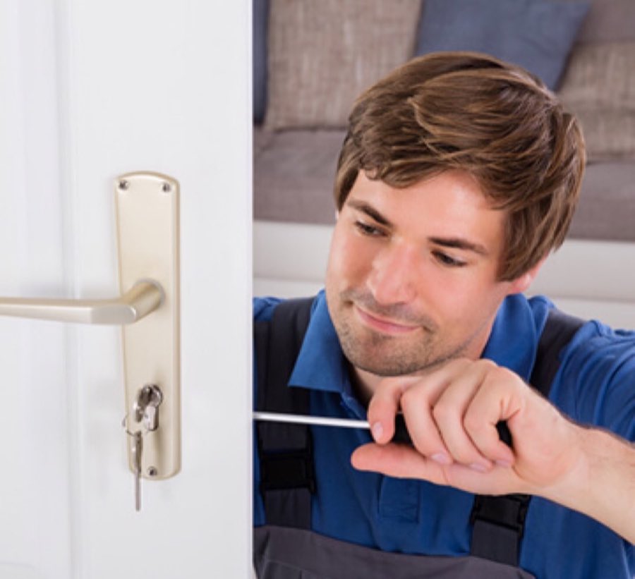 A technician's hand using a screwdriver to service a door lock and handle set indoors