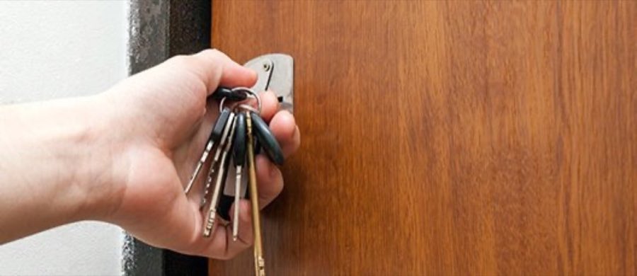 A hand fitting a set of keys into a wooden front-door lock