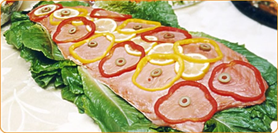 A whole salmon side on romaine decorated with rings of red and yellow pepper, lemon, and olives for a catered platter