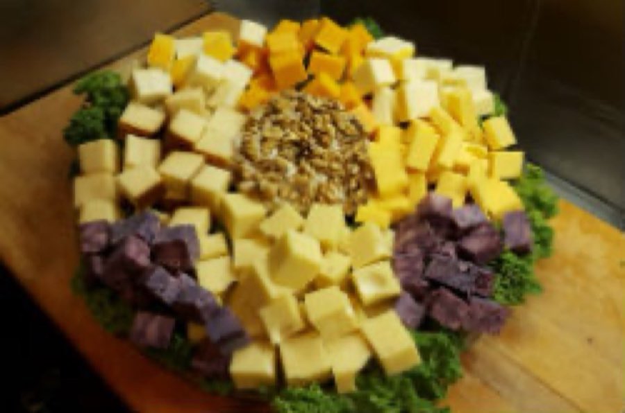 A cheese board cubed and arranged by color with walnuts at the center, on a wooden platter