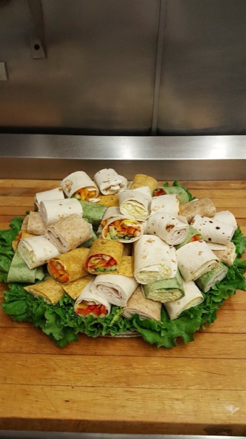 A tiered platter of assorted deli wraps in plain, spinach, and tomato tortillas on a bed of lettuce
