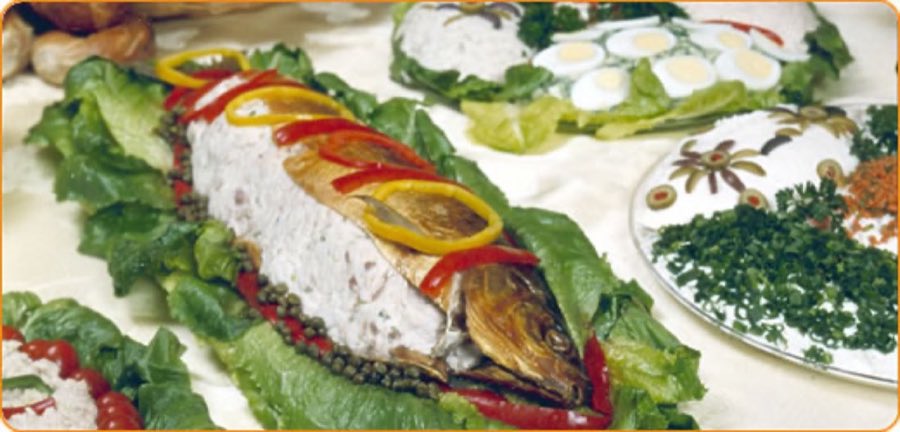 A whole decorated whitefish-salad platter shaped like a fish, ringed with romaine, capers, and red and yellow pepper rings, beside egg-and-herb salad platters