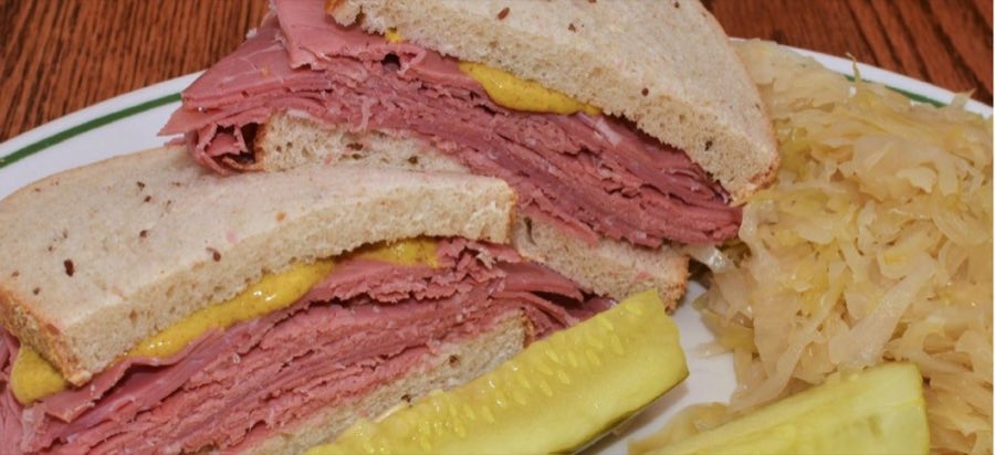 A hand-cut pastrami sandwich on rye with mustard, a pickle spear, and sauerkraut on the side