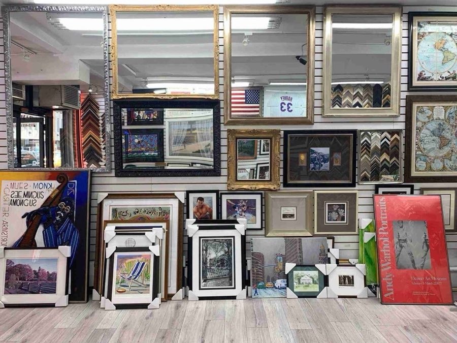 A second interior wall with large mirrors, more of the Mets jersey and flag grouping, an Andy Warhol Portraits museum poster, and framed cityscape paintings, with more art leaning on the floor