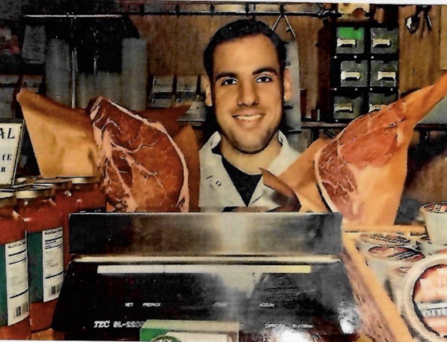 A young Ottomanelli butcher smiling behind the counter scale, holding up two large cuts of prime beef