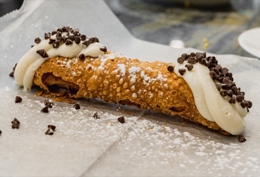 A freshly filled cannoli with chocolate-chip ends and a dusting of powdered sugar, resting on parchment paper