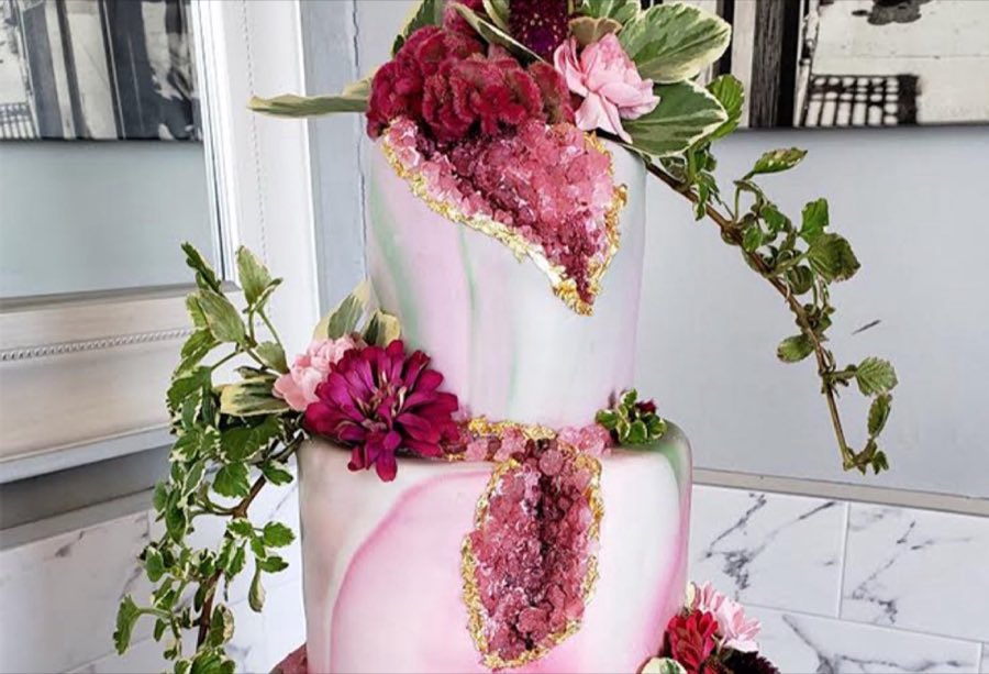 A two-tier pink-and-green marbled geode wedding cake with fresh flowers and gold-leaf accents