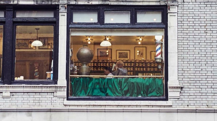 The Paul Molé Barber Shop storefront window on Lexington Avenue, with a red, white, and blue barber pole and a barber attending a seated client inside