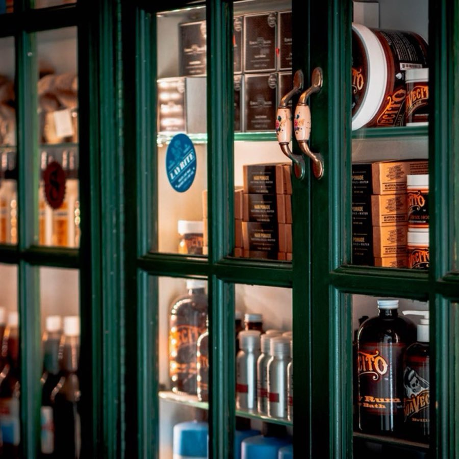 A forest-green display cabinet holding the shop's grooming products, pomades, and tonics