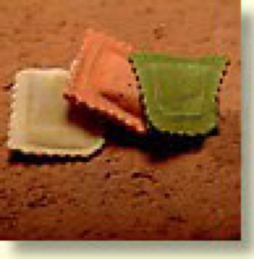 Three ravioli in cream, tomato, and spinach dough on a wooden board