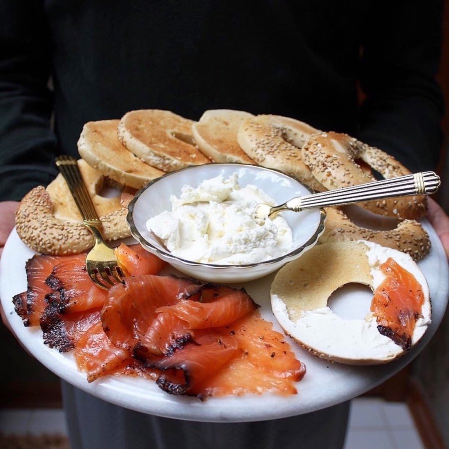 Close-up of an everything bagel piled high with smoked salmon, tomato, red onion and cream cheese, on a plate at a café table
