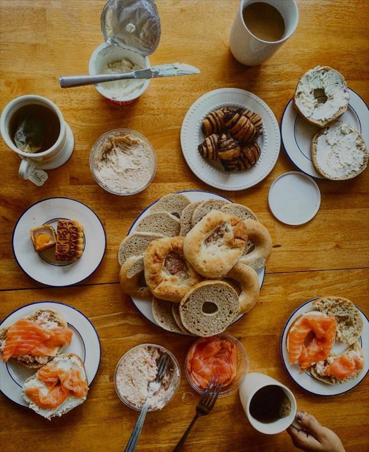 Overhead flat-lay of a full Sable's breakfast spread on a wood table: everything and plain bagels, lox on bagel halves with cream cheese, chocolate babka, cream cheese tubs, coffee and tea