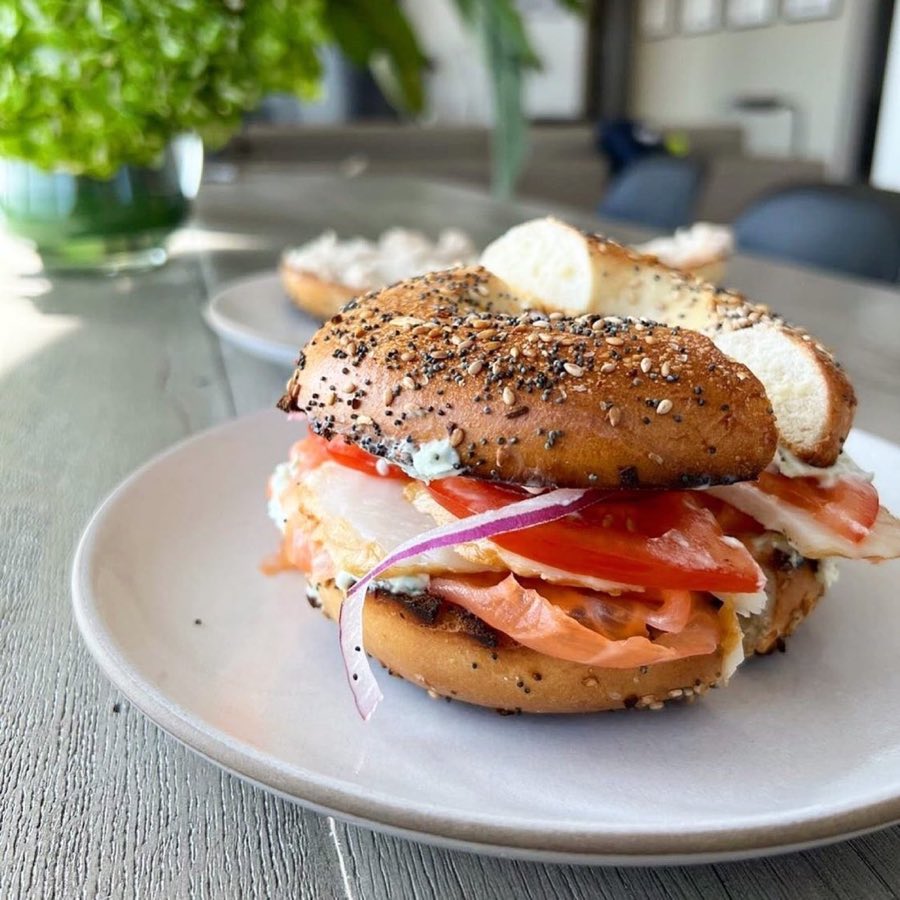 A person holding a large platter of toasted bagels, a bowl of cream cheese, and charred smoked salmon slices, prepared for catering