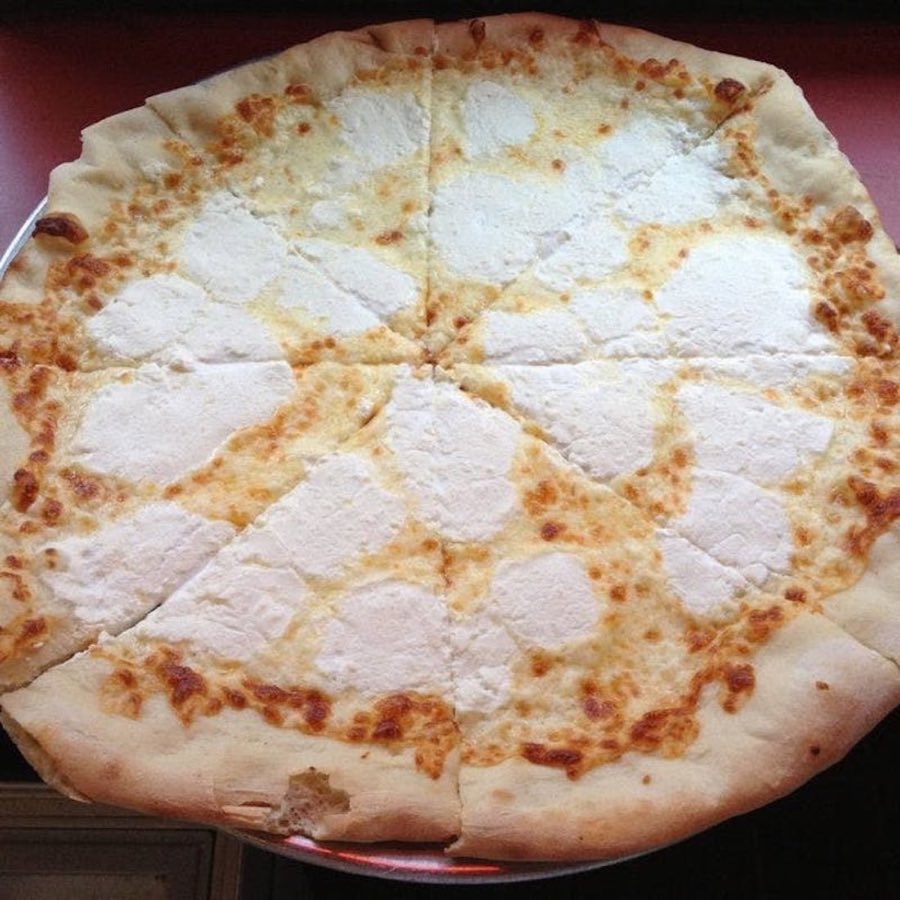 A whole ricotta pizza sliced into eighths, with visible dollops of ricotta