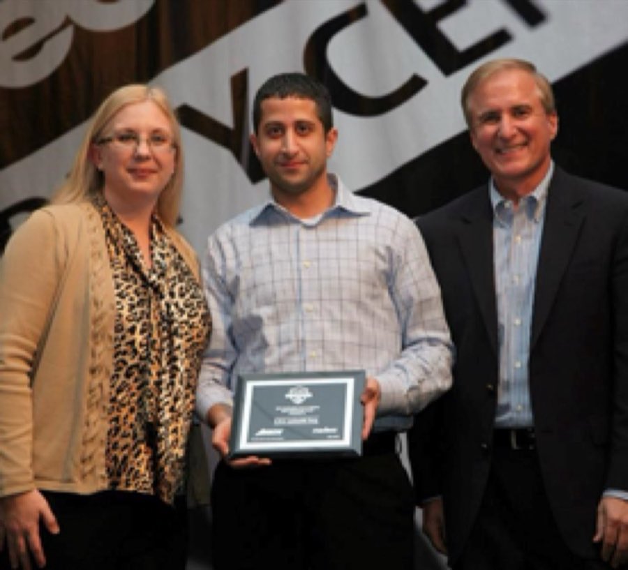 Three people on stage at an industry event; a member of the SOS team stands in the center holding a framed Medeco dealer award plaque, in front of a banner reading Security Center.