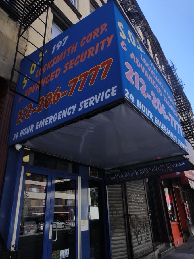 The SOS Locksmith storefront on 7th Avenue in Chelsea: a blue awning with red and gold lettering reading S.O.S. 197 Locksmith Corp. & Advanced Security, 212-206-7777, 24 Hour Emergency Service, above a blue-painted brick storefront.