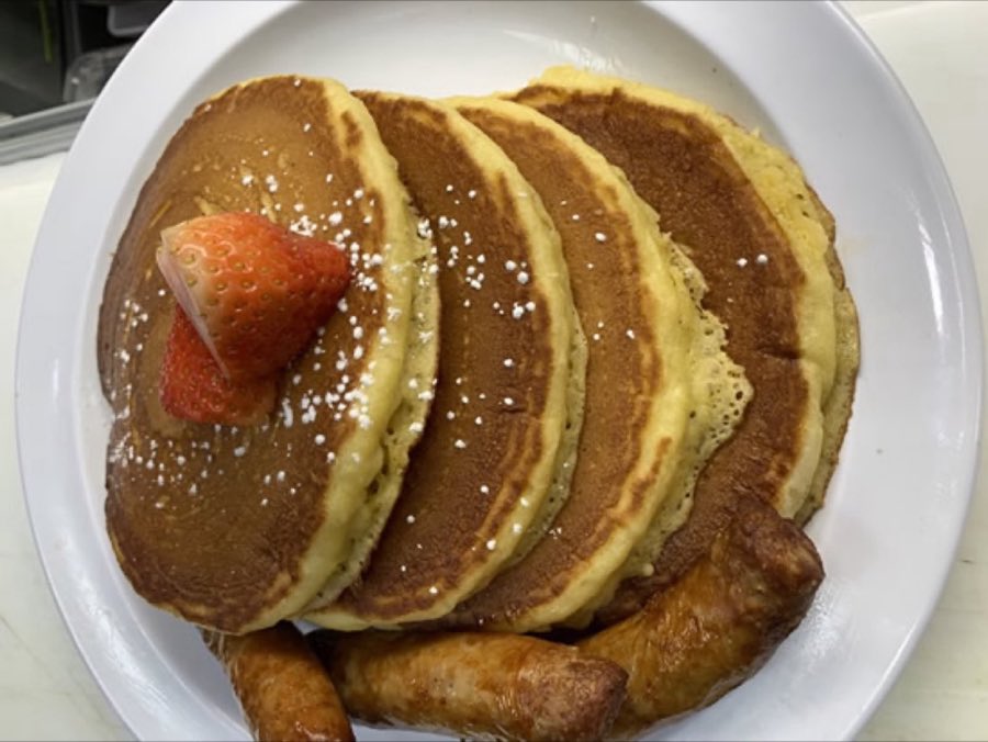 Three golden pancakes topped with sliced strawberries and powdered sugar