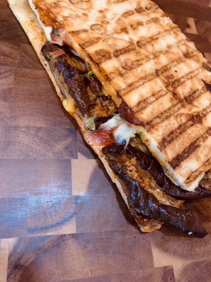 Pressed panini sliced open on a wood board, showing melted cheese and grill marks