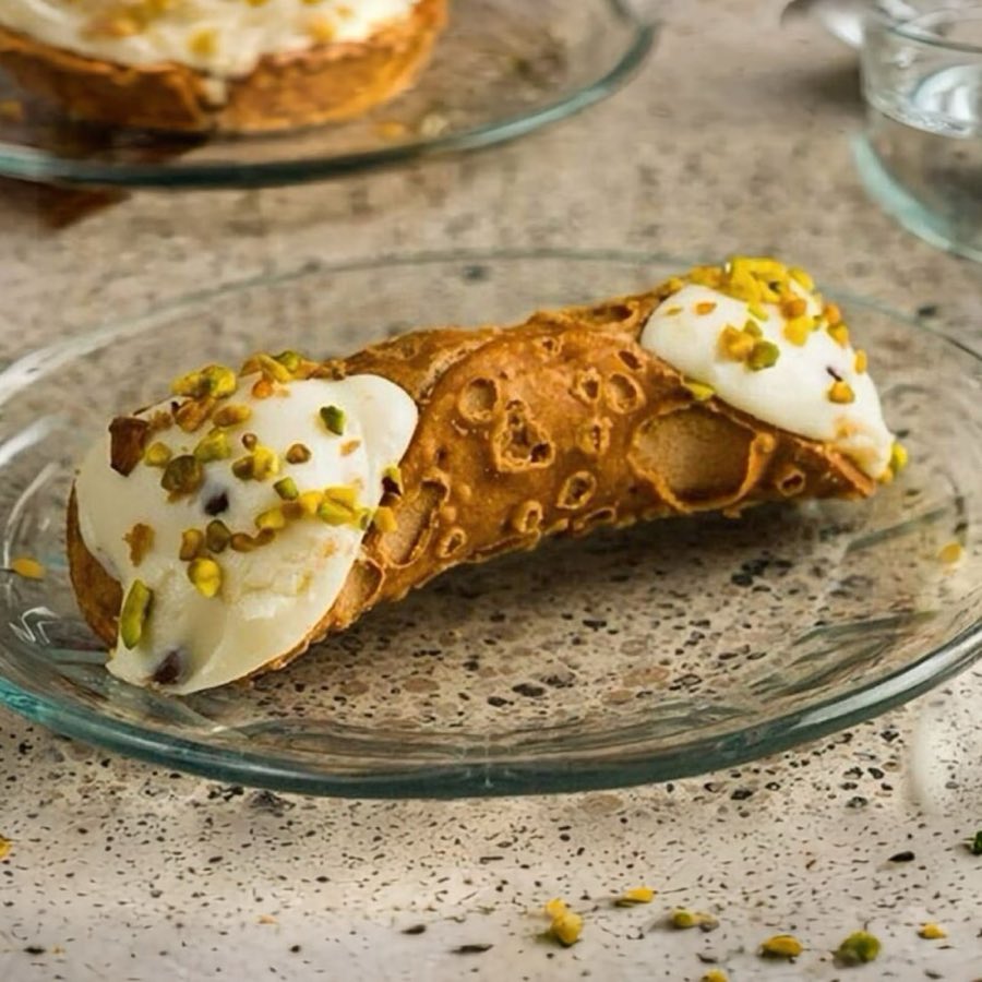 A crisp cannoli shell filled with ricotta cream, topped with crushed pistachio, plated on a marble café table