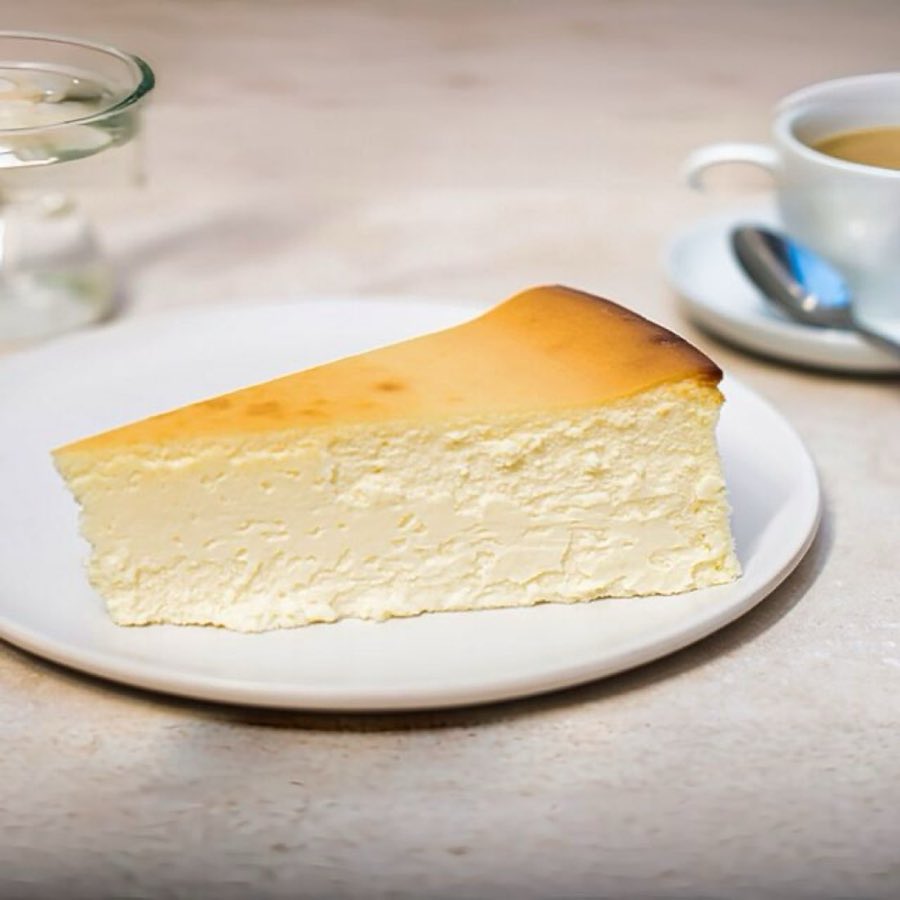 A slice of Veniero's classic New York cheesecake on a white plate at a café table, with espresso in the background