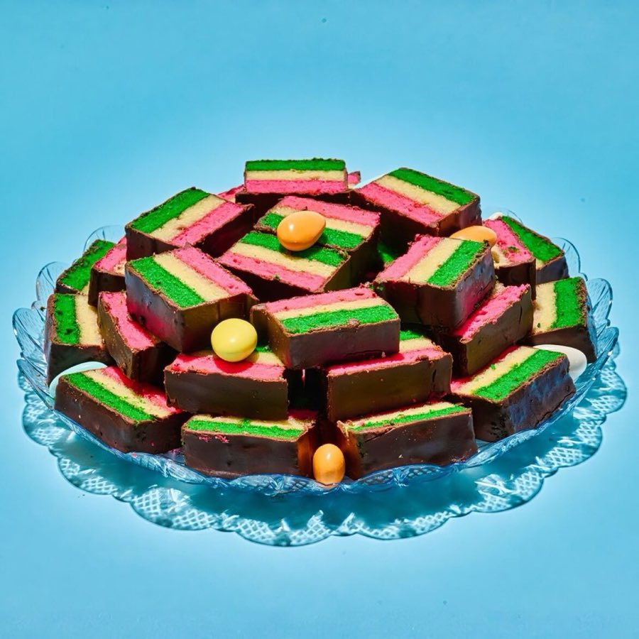 Chocolate-dipped Italian rainbow cookie squares, layered pink, white and green, on a glass tray