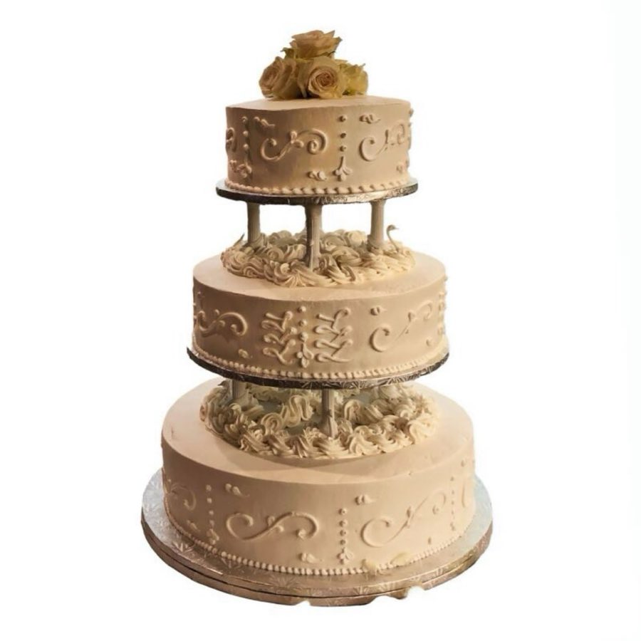 A three-tier round wedding cake with piped scroll and dot buttercream detail, cream roses on top, set on a pedestal stand