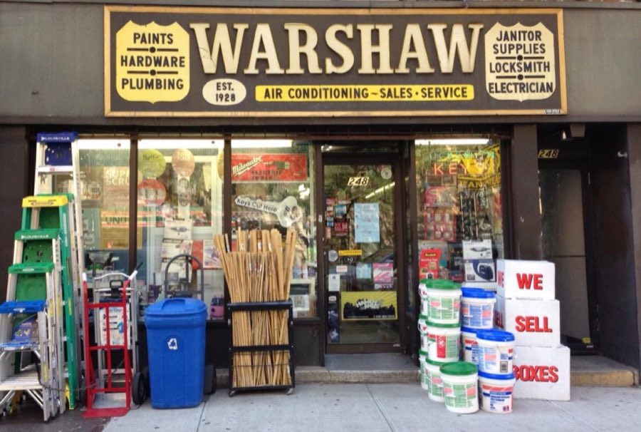 Warshaw Hardware storefront at 248 Third Avenue: a dark sign reading Paints, Hardware, Plumbing, Janitor Supplies, Locksmith, Electrician, Air Conditioning — Sales · Service, with ladders, a hand truck, paint buckets, and boxes for sale on the sidewalk out front