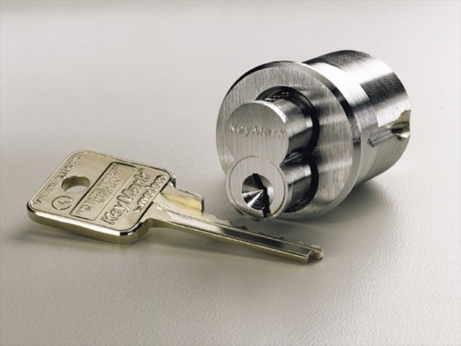 A KeyMark brass door lock cylinder and its cut key on a plain background