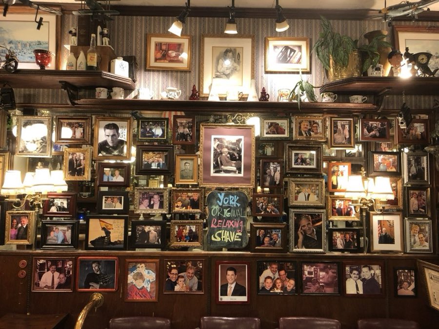 Wall inside York Barbershop covered floor to ceiling with vintage framed photographs, brass sconces, and a hand-painted sign reading York Original Relaxing Shave