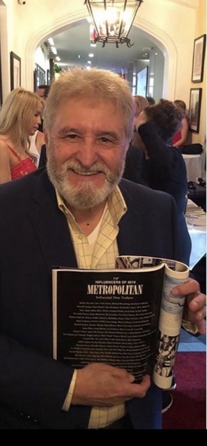 Enrique, York Barbershop stylist, bearded and smiling, holding a magazine feature on New York influencers